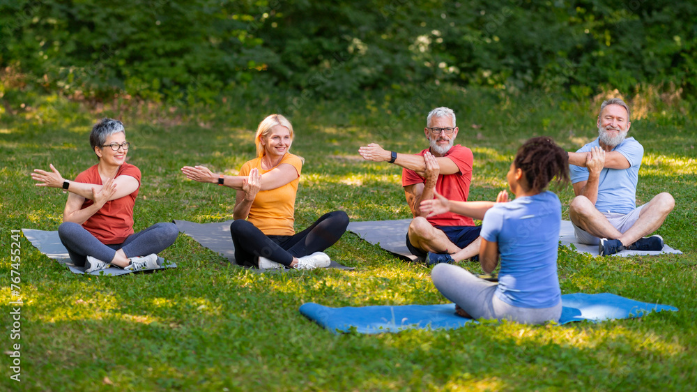 Enthusiastic group of seniors following yoga instructor's movements while training outdoors