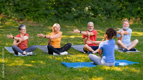 Enthusiastic group of seniors following yoga instructor's movements while training outdoors