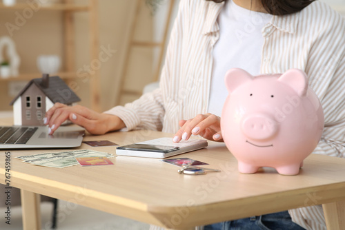 Woman with piggy bank, laptop and house model at home. Mortgage concept