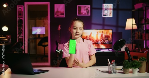 Cute kid filming internet show, promoting green screen tablet received from sponsoring brand. Little girl does influencer marketing, urging followers to purchase chroma key device