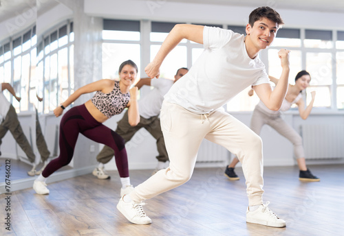 Group of young people, girls and guys in sportive casual style clothes dancing in choreography class