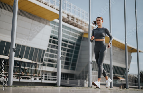 Active young woman in athletic wear jogging in a modern city environment, showcasing a healthy lifestyle and determination.
