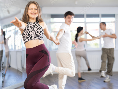 Cheerful enthusiastic young girl rehearsing upbeat jive dance moves with male partner in bright studio. Active hobby concept..