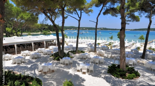  a bunch of tables and chairs are set up on the sand near the water with boats in the water behind them.