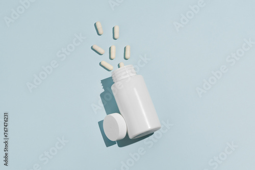 White mockup jar with spilled pills tilted on blue isolated background. Concept of pharmacy, medicine, dietary supplements and health. Image for your design