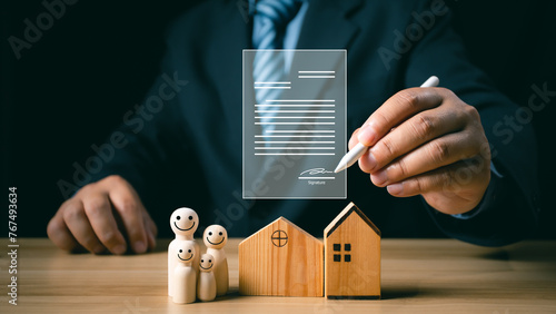 Businessman signing a lease or buying a house, wooden house and wooden doll on the table, The concept of family planning, loan, mortgage, property or home, sale purchase deal.