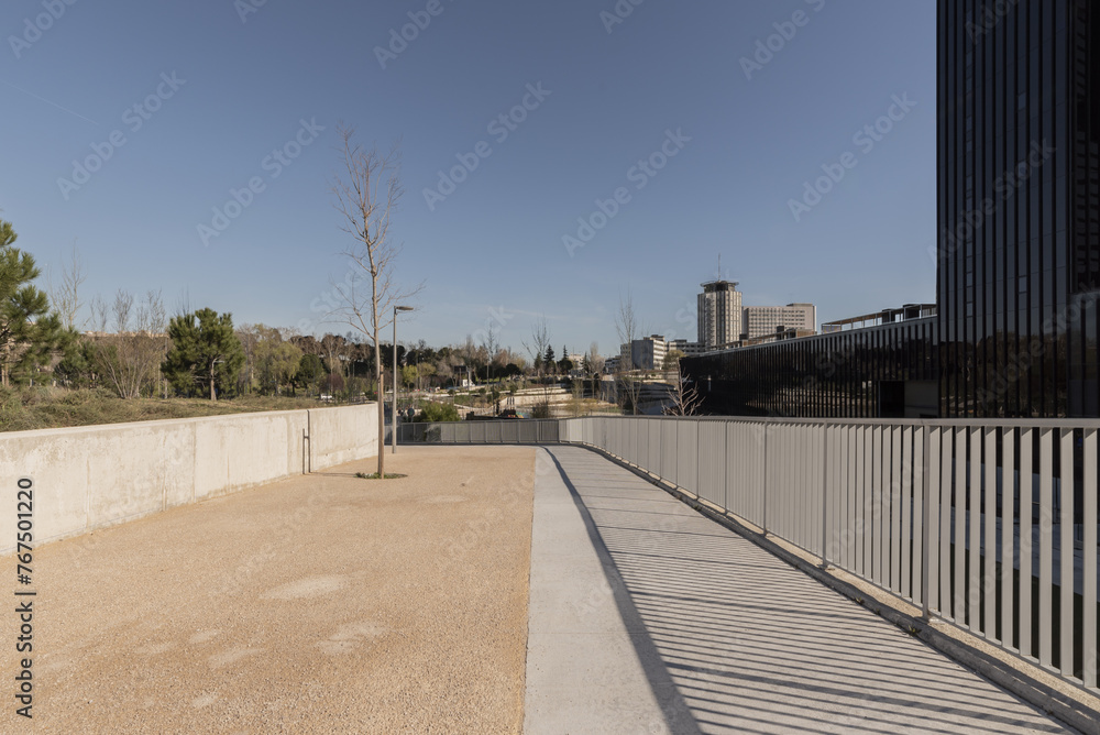 A walk in a park with long railing next to the ground floor of a skyscraper tower