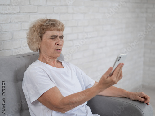 An elderly Caucasian woman suffers from farsightedness and tries to read a message on a smartphone with her arm outstretched.  photo