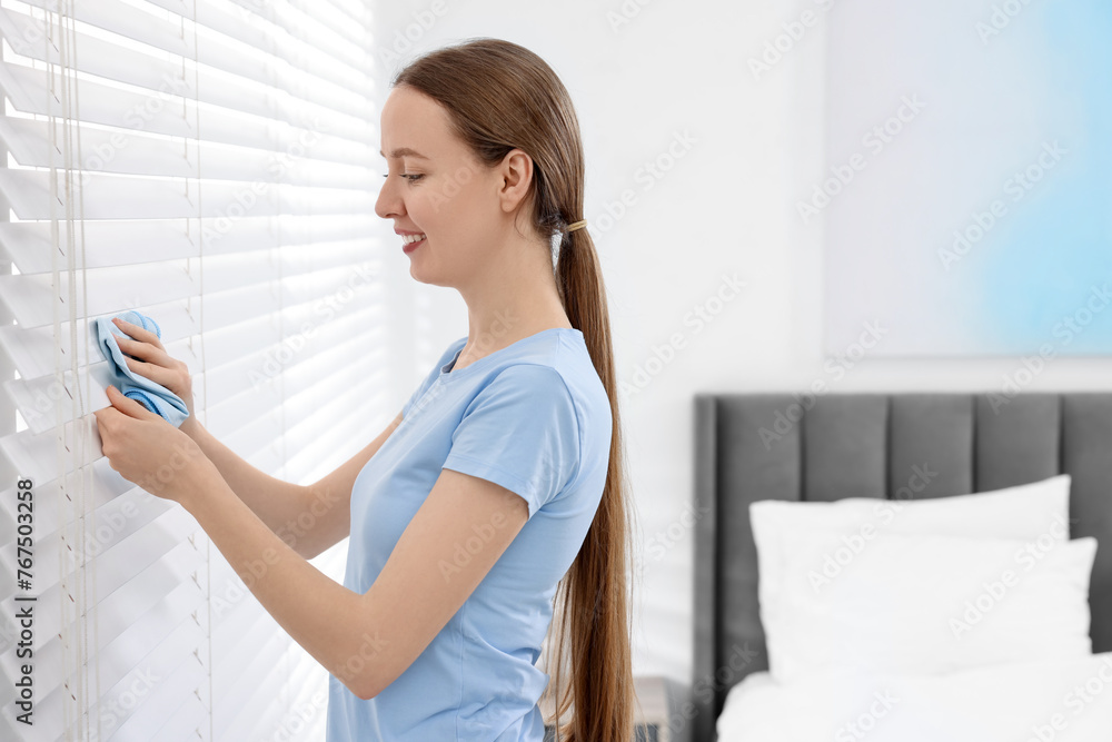 Woman with microfiber cloth wiping blinds at home. Space for text Woman with microfiber cloth wiping blinds at home. Space for text