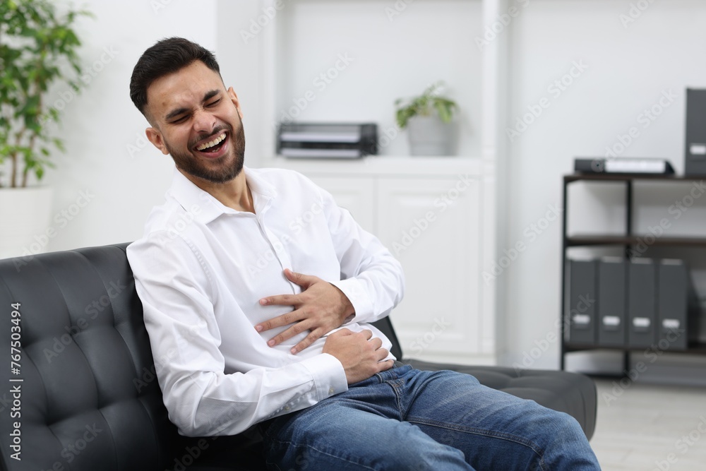 Handsome young man laughing on sofa in office