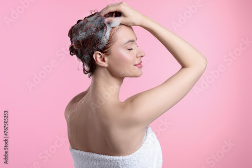 Happy young woman washing her hair with shampoo on pink background