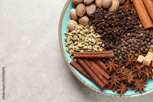 Different spices and nuts in bowl on light gray textured table, top view. Space for text