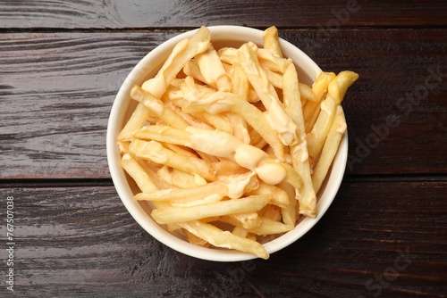 Delicious french fries with cheese sauce in bowl on wooden table, top view