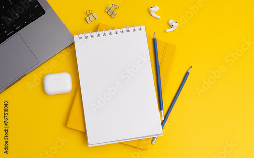 Top view composition with yellow notebook and pens placed near laptop and headphones on yellow background (ID: 767518048)