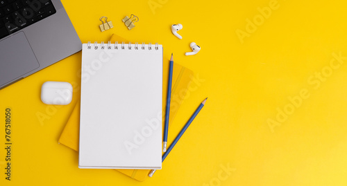 Top view composition with yellow notebook and pens placed near laptop and headphones on yellow background (ID: 767518050)