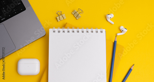 Top view composition with yellow notebook and pens placed near laptop and headphones on yellow background (ID: 767518052)
