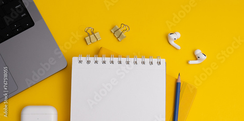 Top view composition with yellow notebook and pens placed near laptop and headphones on yellow background (ID: 767518055)