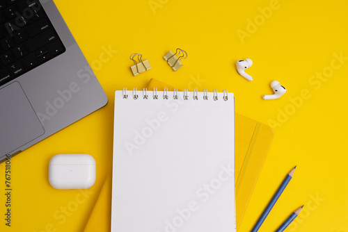 Flat lay, top view yellow table. Workspace with notebook, keyboard, office supplies, pencil, headphones. (ID: 767518066)