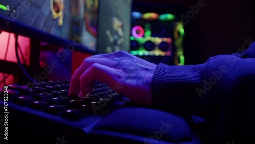 Gamer typing on backlight keyboard close-up, man playing video game in blue neon light . Male hands pushing buttons on computer mouse. having a stream, cyberspace. photo