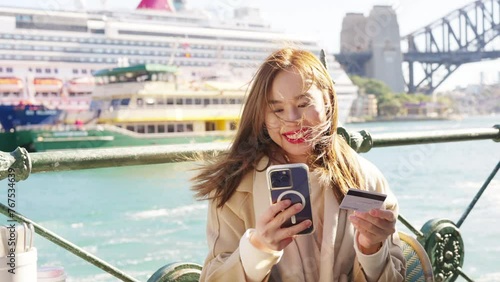 Asian woman using mobile phone with credit card booking hotel or online shopping during travel in Australia. Attractive girl enjoy outdoor lifestyle travel and shopping in the city on holiday vacation