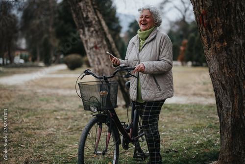 Mature woman with bicycle standing in a park, looking at her phone during a leisure activity.