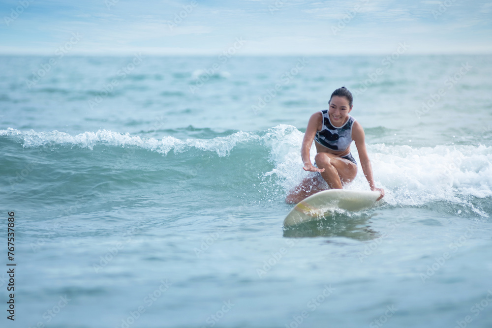 Asian surfing woman riding the waves on sunny day, outdoor activities, water sports activities concept