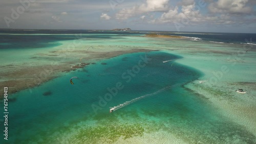 Kitesurfers gliding over a clear turquoise sea with a coral reef, aerial view