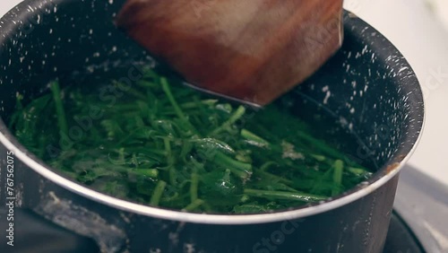 Using a wooden spatula to stir pot of boiling water blanching fiddlehead ferns for making pako salad, a local Filipino delicacy showing the authentic daily home life and culinary heritage photo