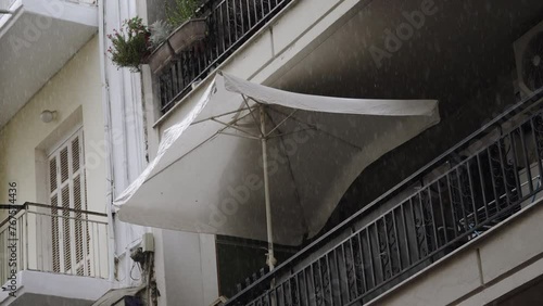 White tent umbrella is opened on balcony of apartment on rainy day. Rainy and humid day in resort town, no people. Bad, abnormally cold weather during summer vacation on the sea coast. photo