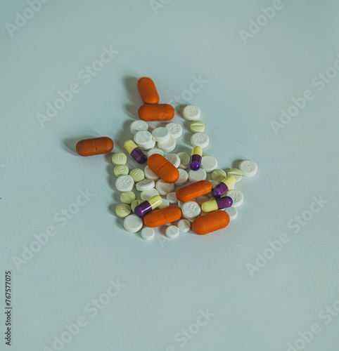 A close-up top view photo of a pile of colorful capsules and round tablets on a white background,