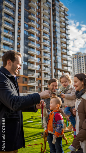 A family of four is standing outside of a building  with a man holding a key and a child holding a leash. Scene is happy and friendly  as the family appears to be enjoying their time together
