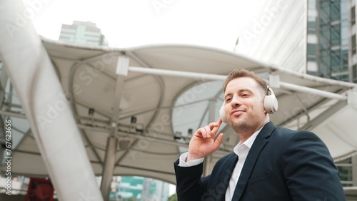 Happy business man using headphone listening relax music and move along music while walking at street in urban city with lively mood. Manager wear headset and enjoying listen relaxing rhyme. Urbane.