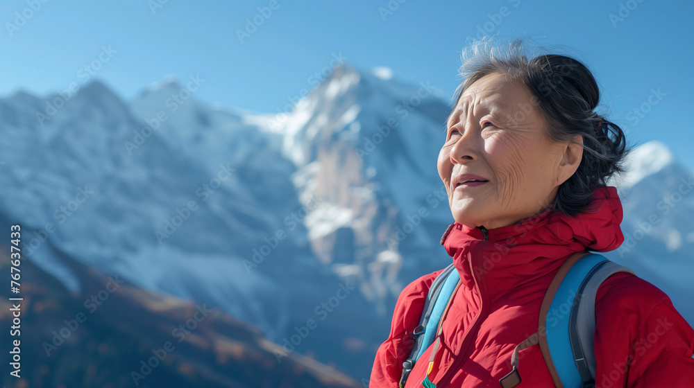  Asian woman in her 60s stands on top of the Alps, looking at the magnificent scenery. She is wearing red mountaineering clothes