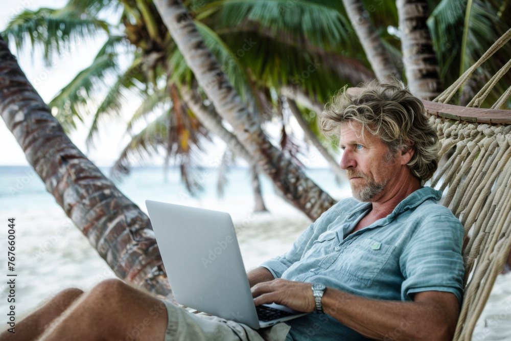 Senior man using laptop while sitting in hammock on a tropical beach
