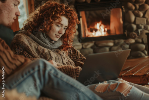 Young red-haired woman using laptop at home in front of fireplace. 