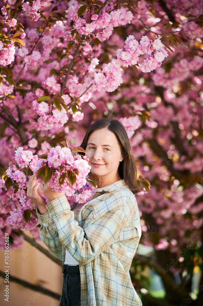 Woman allergic enjoying after treatment from seasonal allergy at spring. Portrait of happy beautiful woman smiling in front of blooming sakura tree at springtime. Spring allergy concept.