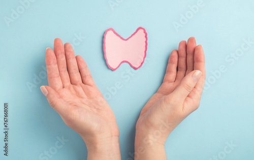 Thyroid gland decorative model in woman hands on pastel blue background. Hyperthyroidism, Hypothyroidism, thyroid cancer awareness concept. Top view photo