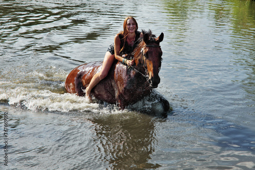 Alluring woman playing with the horse in the summer lake