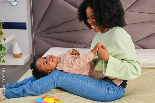 Cuban mother tickled her toddler daughter who is laughing on bed. photo