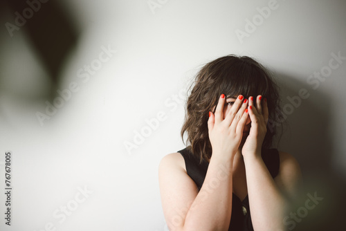 Woman peaks through fingers while looking at camera, copy space photo