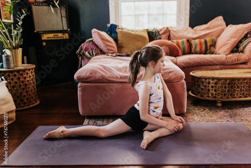 Side view of young girl doing pigeon pose in living room photo