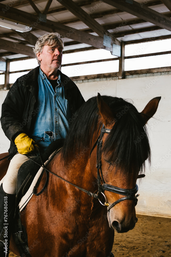 Older man riding on chestnut stallion horse with side light Older man riding on chestnut stallion horse with side light