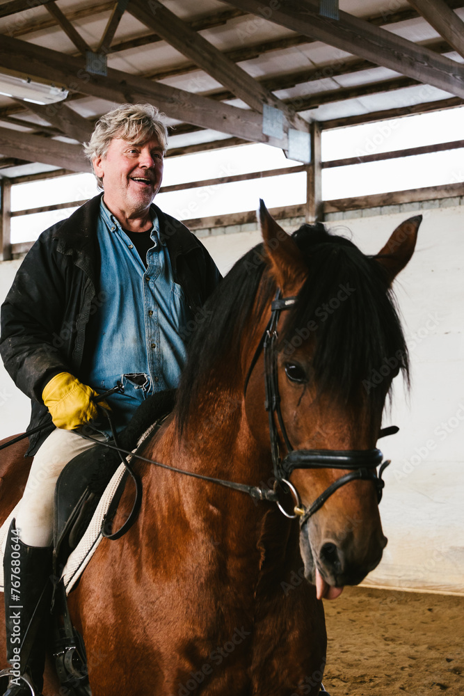 Gray haired older man riding a chestnut stallion indoor arena Gray haired older man riding a chestnut stallion indoor arena