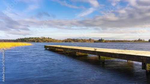 Time lapse of a concrete lake pier in the foreground and castle ruin island with forest in distance on a cloudy sunny day at Lough Key in county Roscommon in Ireland. photo