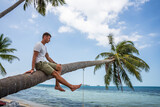Mężczyzna na rajskiej plaży siedzi na palmie