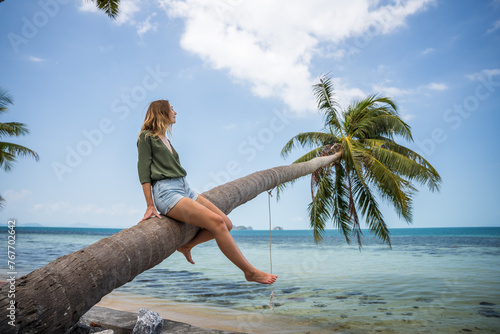 Kobieta siedzi na palmie nad wodą na rajskiej plaży © DawidFastMan