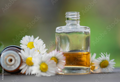 bottles of essential oil and daisies with fresh mint leaf on a wooden table  ...