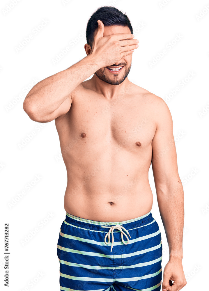 Young handsome man wearing swimwear smiling and laughing with hand on face covering eyes for surprise. blind concept. Young handsome man wearing swimwear smiling and laughing with hand on face covering eyes for surprise. blind concept.