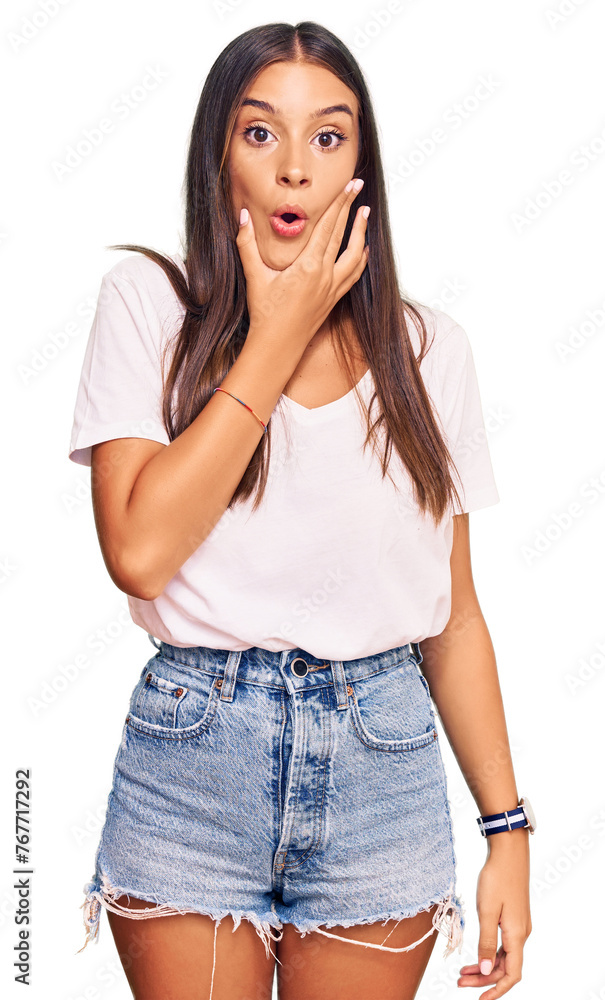 Young hispanic woman wearing casual white tshirt looking fascinated with disbelief, surprise and amazed expression with hands on chin Young hispanic woman wearing casual white tshirt looking fascinated with disbelief, surprise and amazed expression with hands on chin