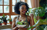 Young black african american woman in sports gear enjoying a green salad. Concept of healthy lifestyle and inclusivity